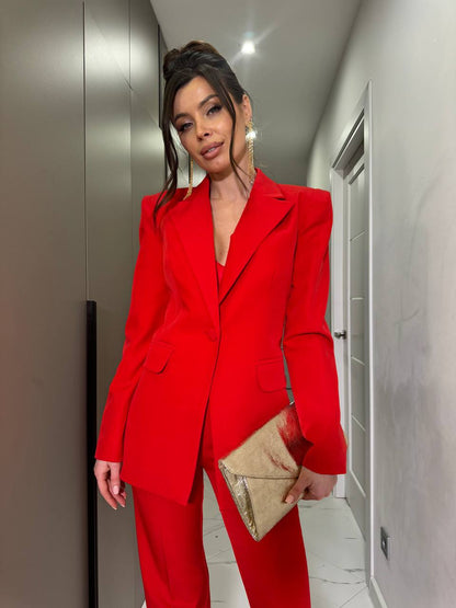 Person wearing a red suit holding a gold clutch in an indoor setting.