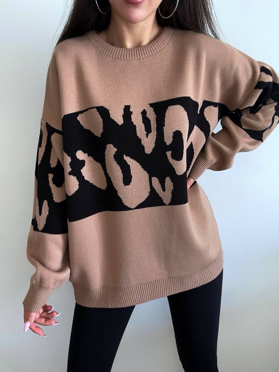 Beige sweater with black abstract pattern worn by a person against a plain background