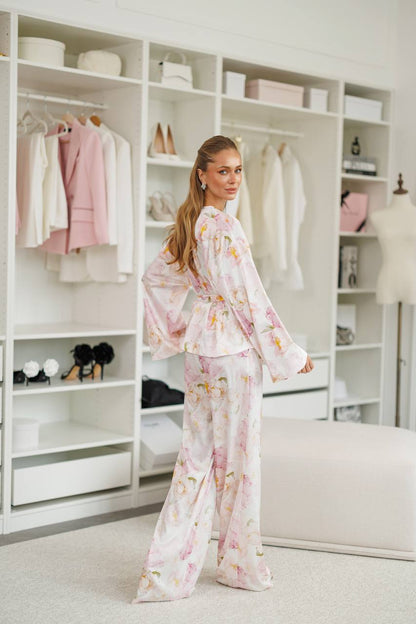 Woman in a floral outfit standing in a stylishly decorated room with shelves and decor.