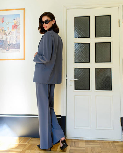 Woman in a gray suit standing in a room with a white door and framed picture on the wall.