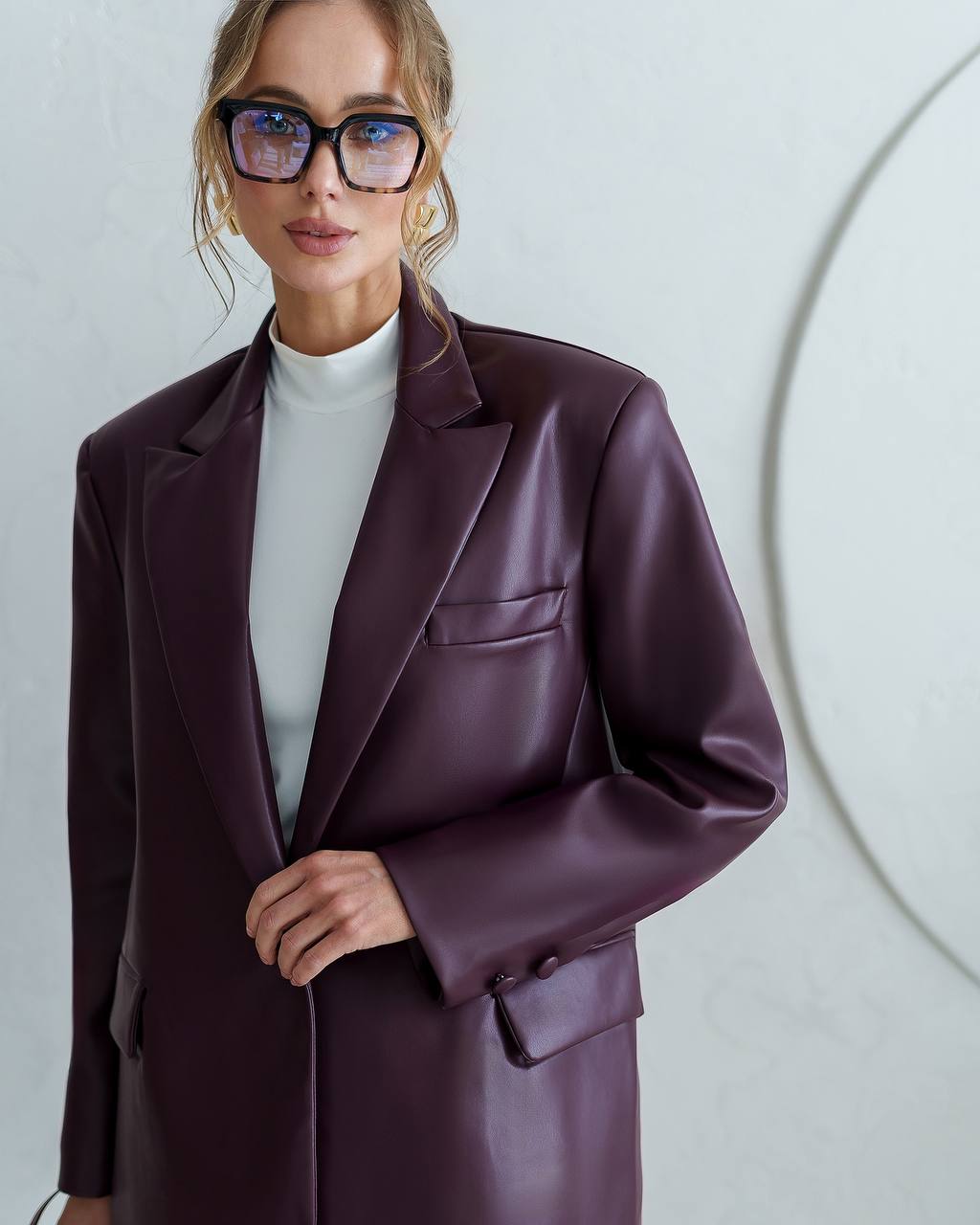 Woman wearing a purple coat and glasses against a plain background