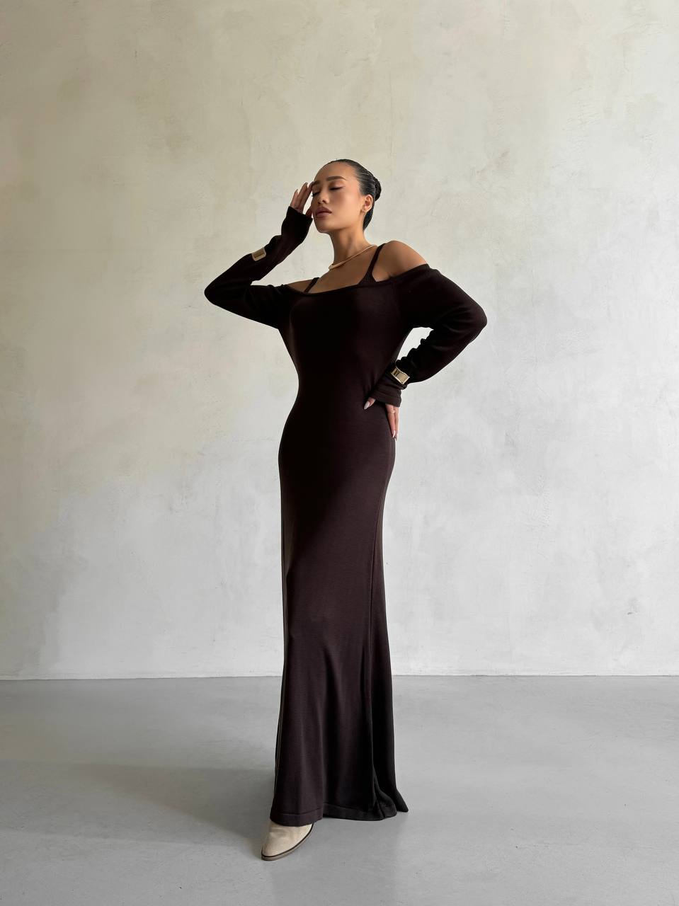 Woman wearing a dark brown off-shoulder dress against a plain background