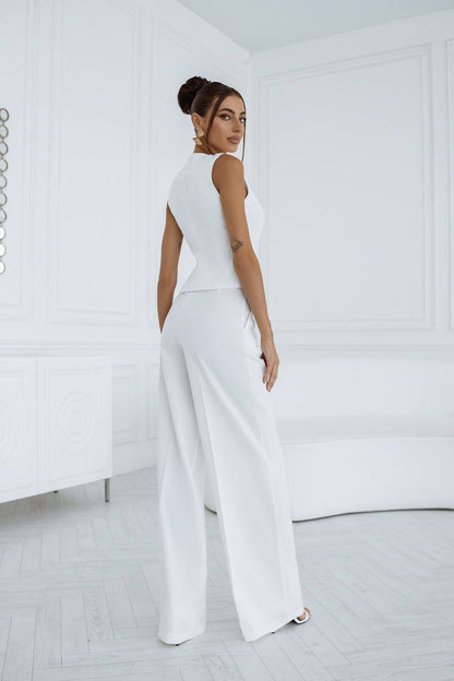 Woman wearing a white sleeveless top and wide-leg pants in a minimalistic room.
