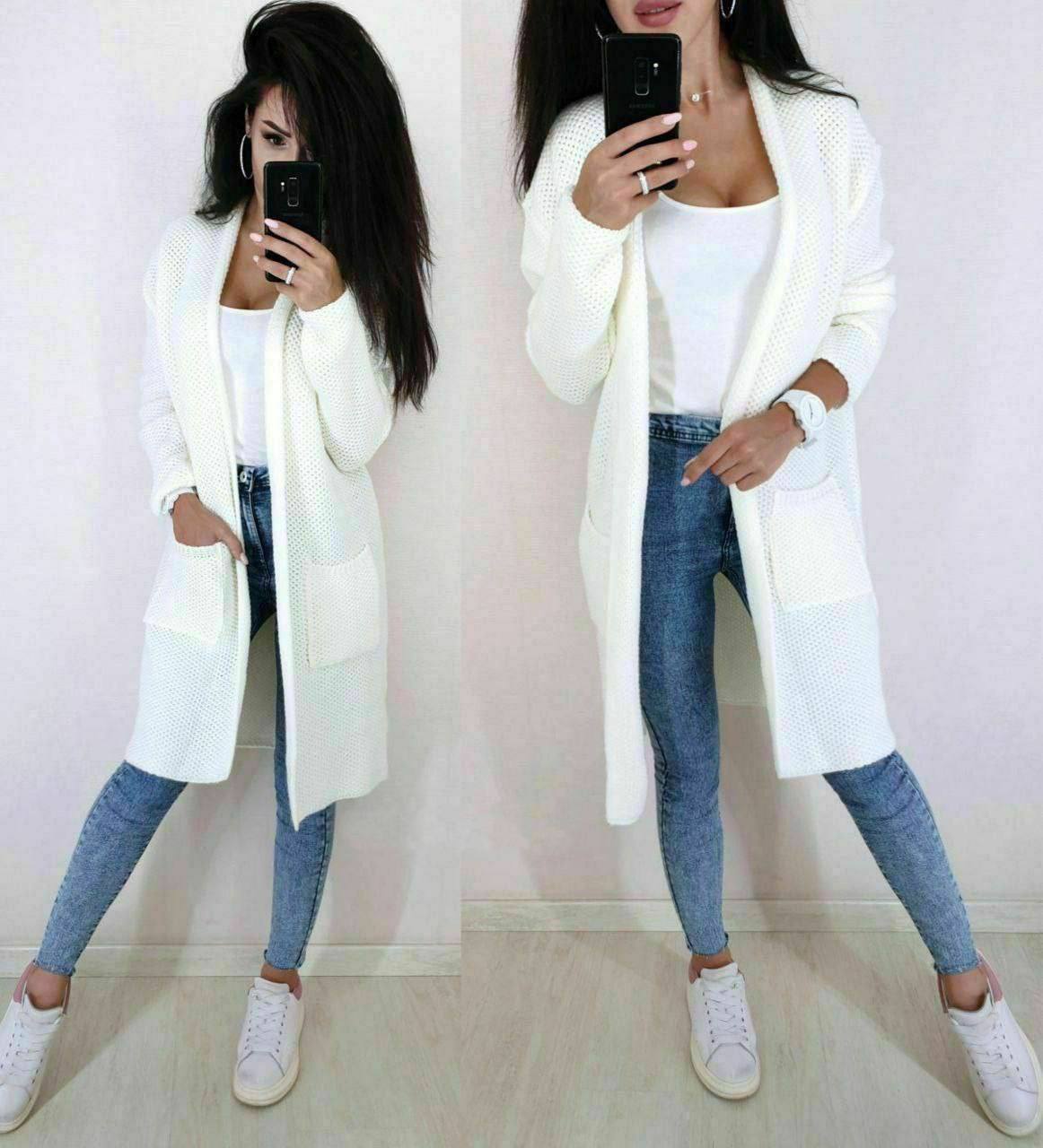 Woman wearing a long white cardigan, white top, blue jeans, and white sneakers.