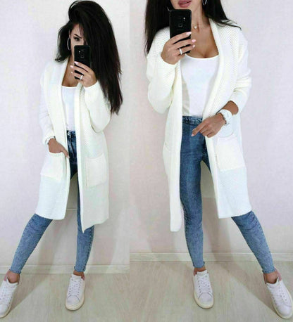 Woman wearing a long white cardigan, white top, blue jeans, and white sneakers.