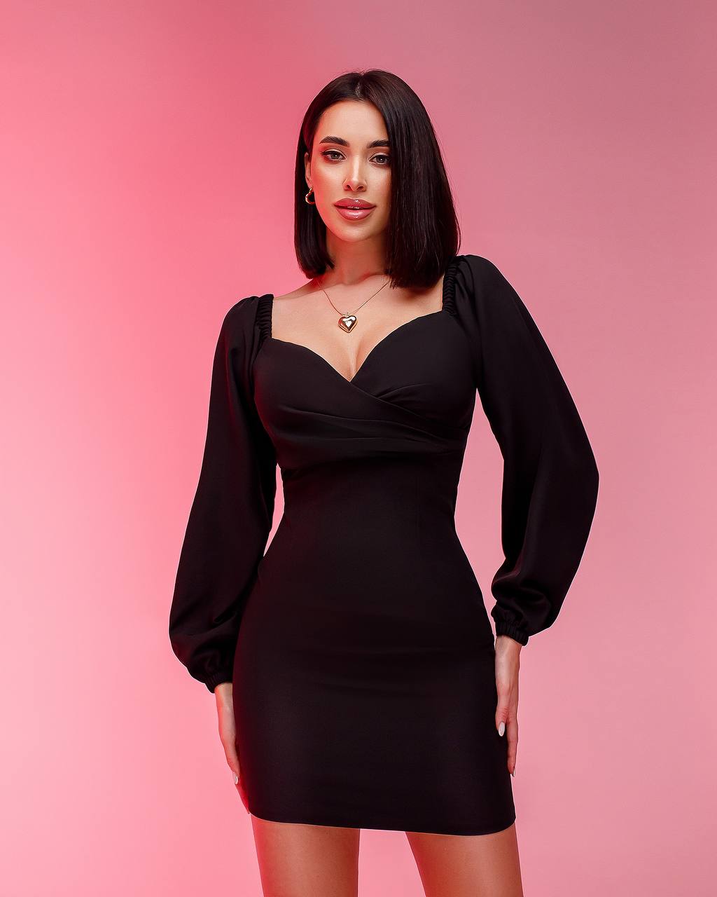 Woman wearing a black dress with long sleeves on a pink background