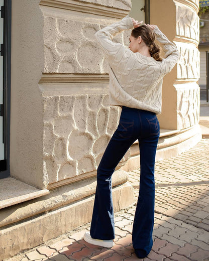 Woman wearing a white sweater and blue jeans standing in front of a stone building.