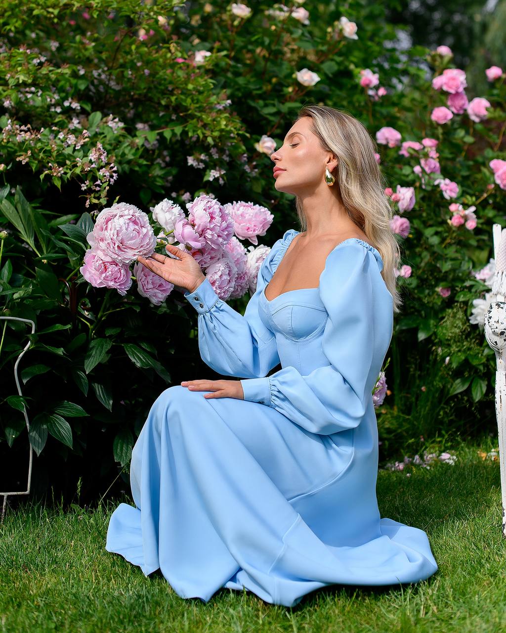 Woman in a light blue dress holding flowers in a garden setting