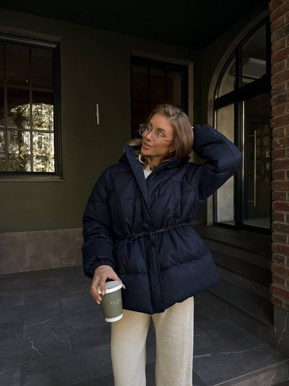 Woman in a navy puffer coat holding a coffee cup outside a building.