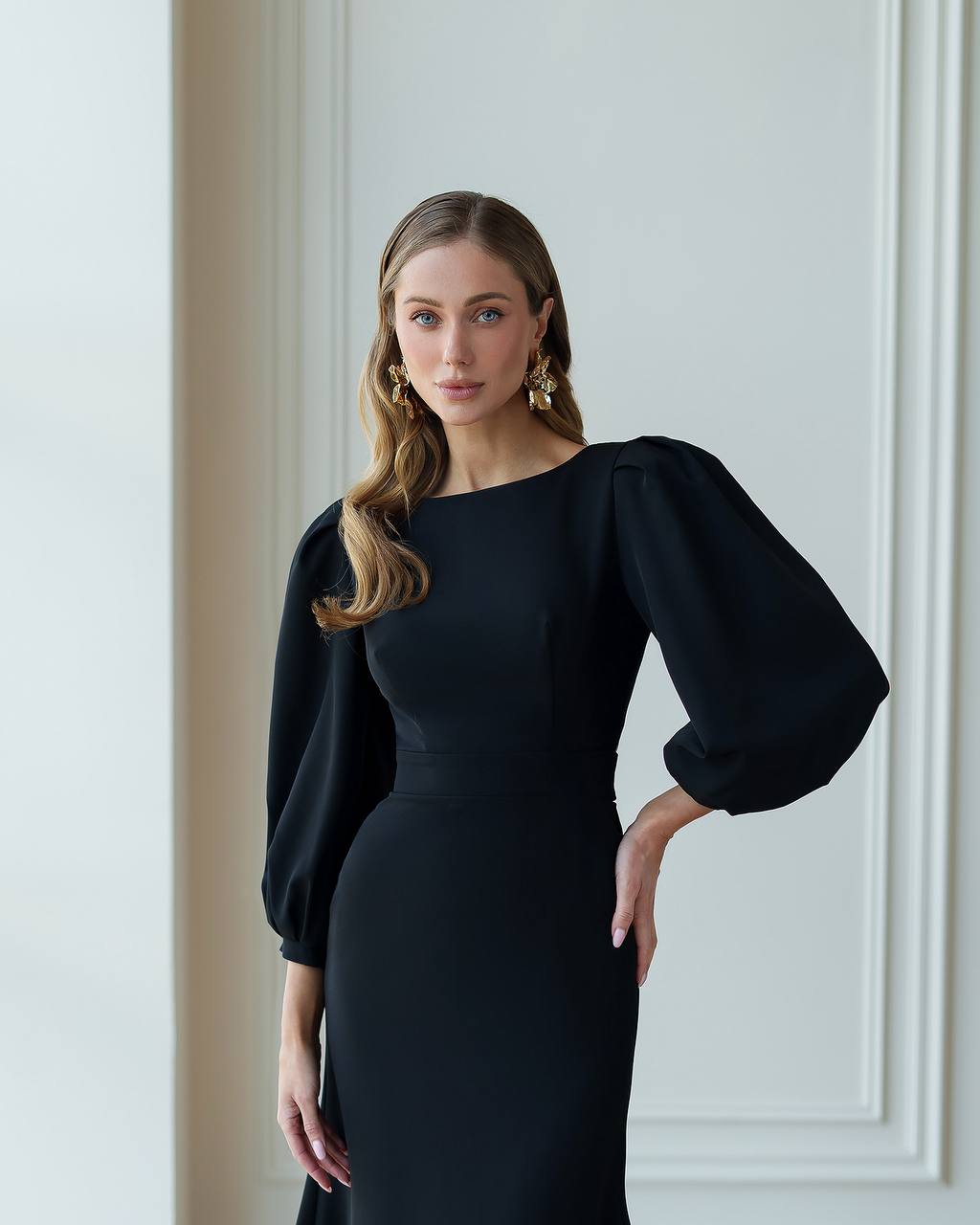 Woman wearing a black dress with puffed sleeves against a white wall