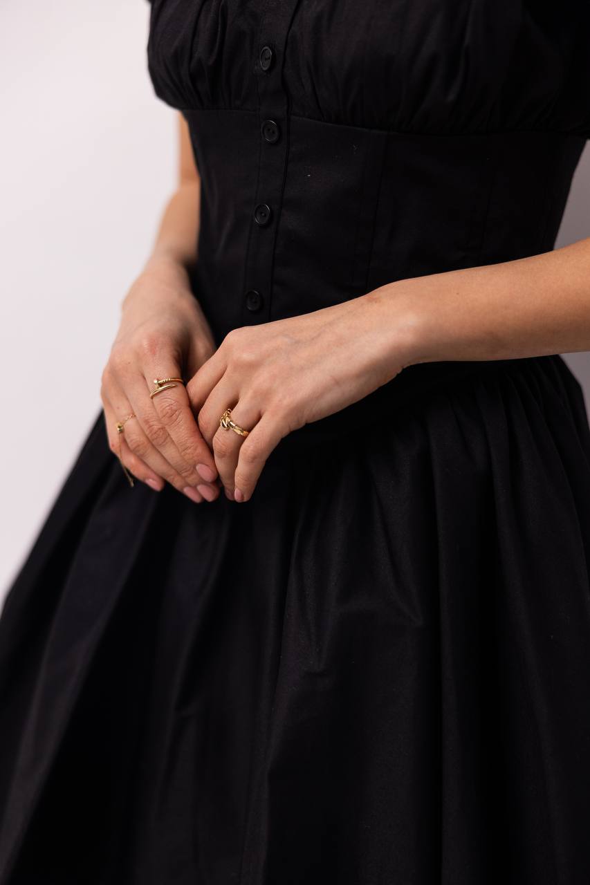 Person wearing a black dress with hands clasped in front, on a plain background