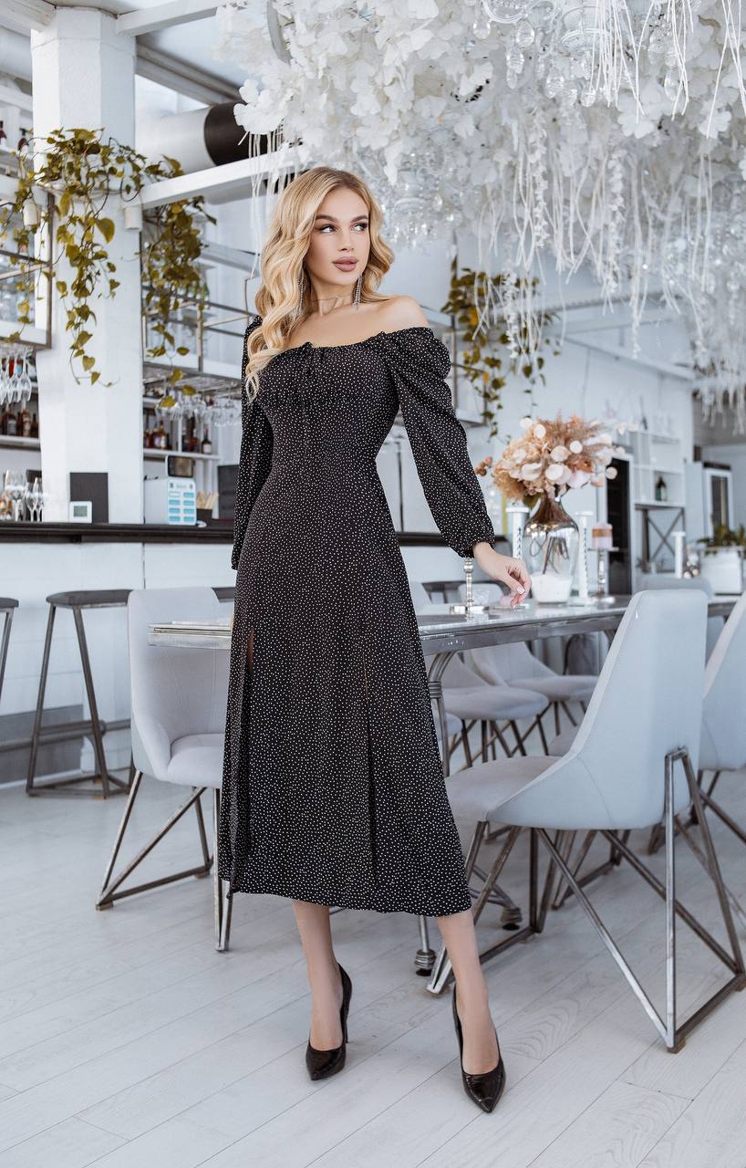 Woman in a black off-shoulder dress standing in a modern restaurant.