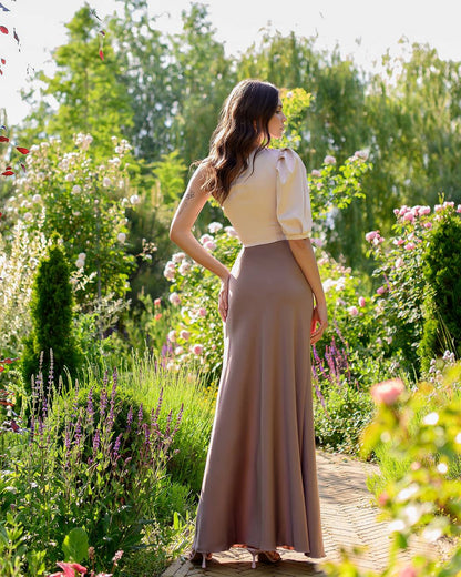 Woman in a long dress standing in a garden with flowers and greenery.