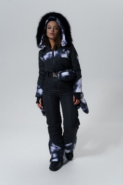 Person wearing a black and white tie-dye jacket with fur hood on a gray background