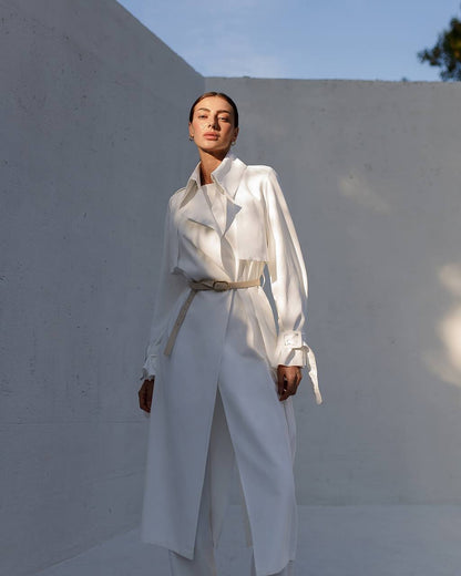 Person wearing a white outfit standing against a light-colored wall.