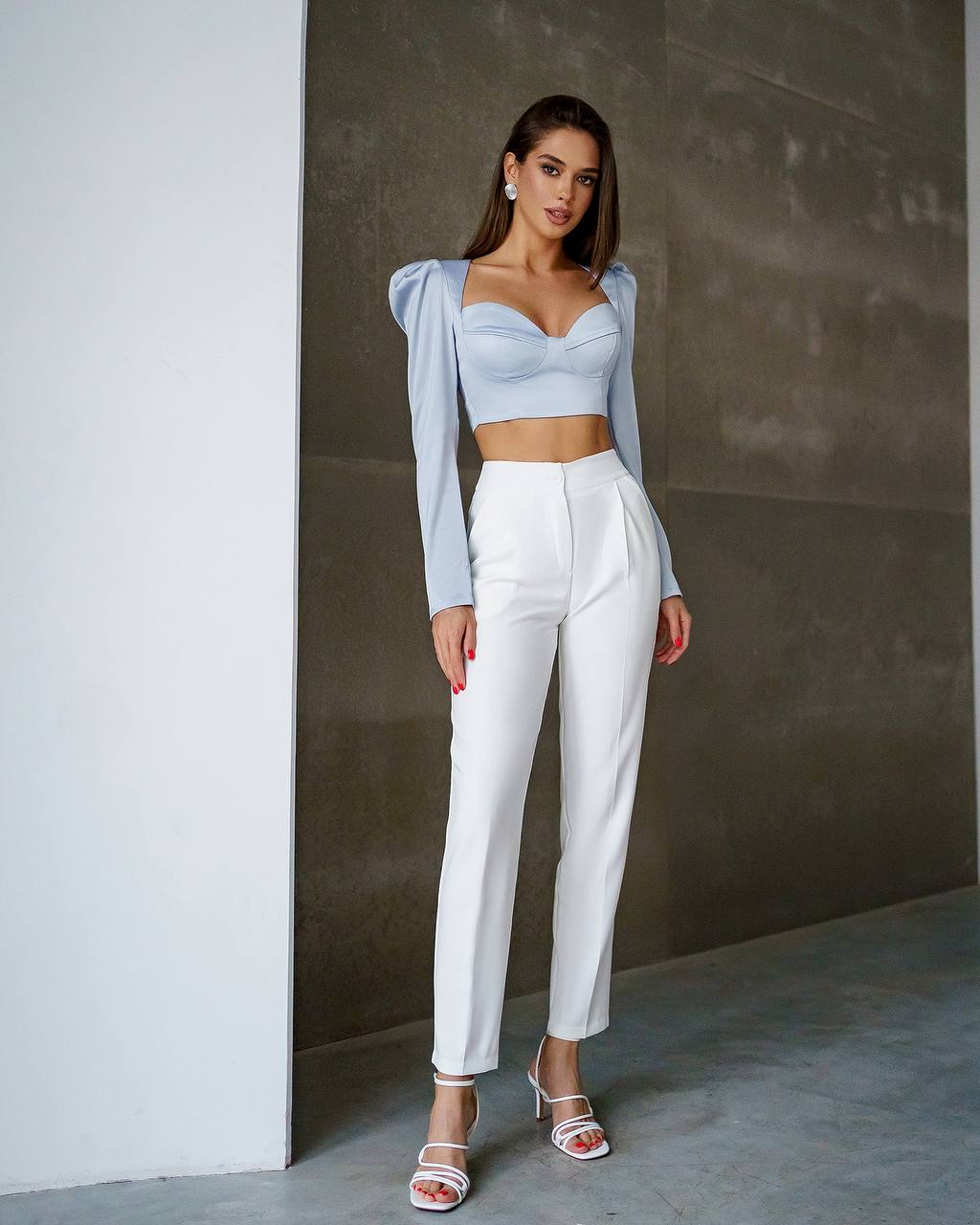 Woman wearing a light blue top and white pants against a neutral background