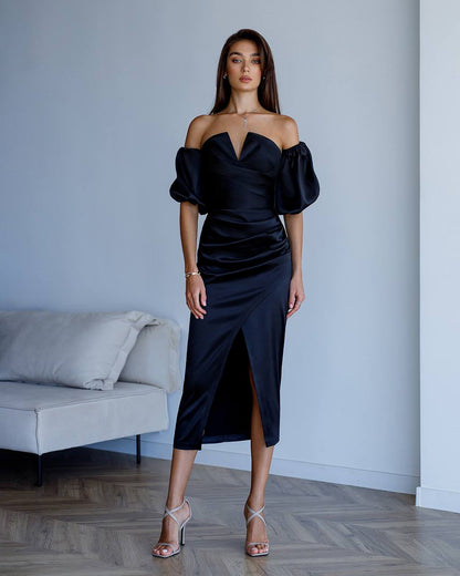 Woman wearing a black off-shoulder dress in a minimalistic room.