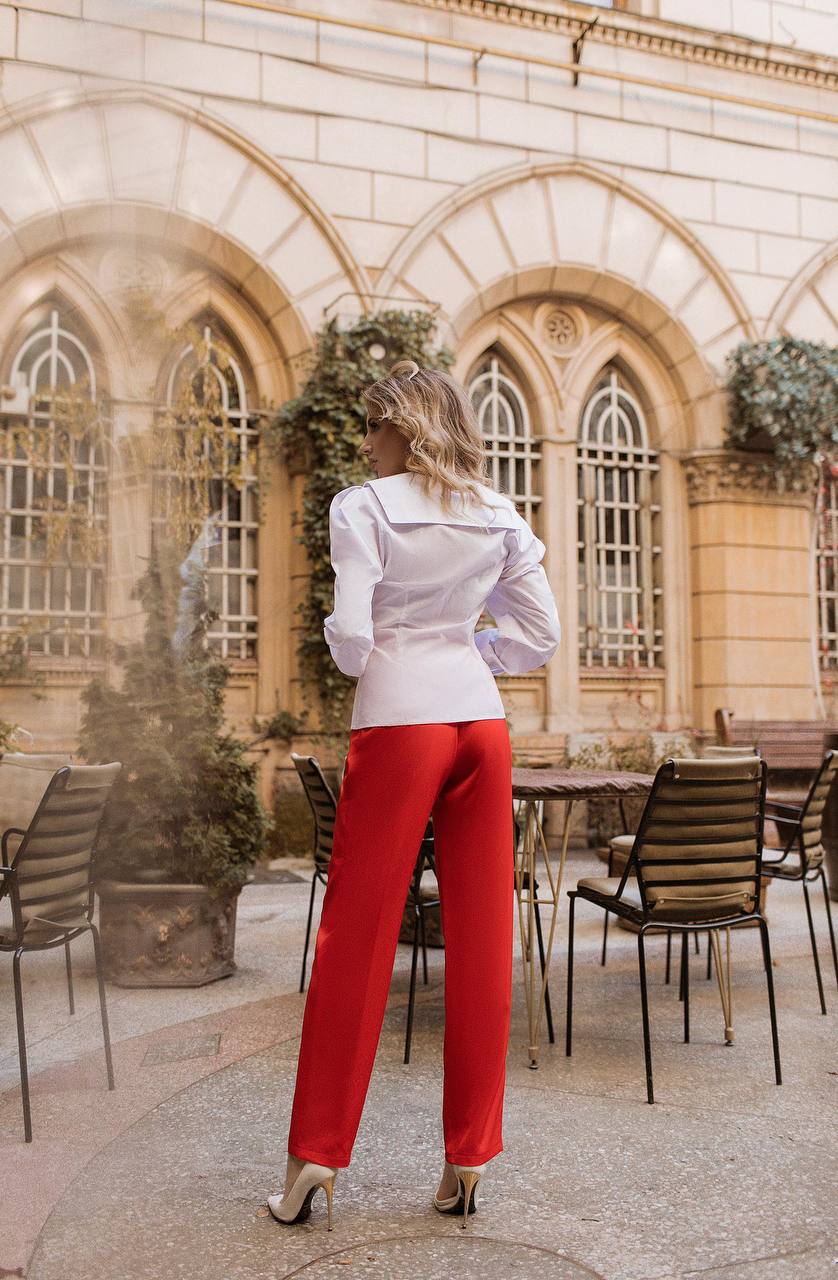 Woman in a white blouse and red pants standing in an outdoor setting with architectural elements.