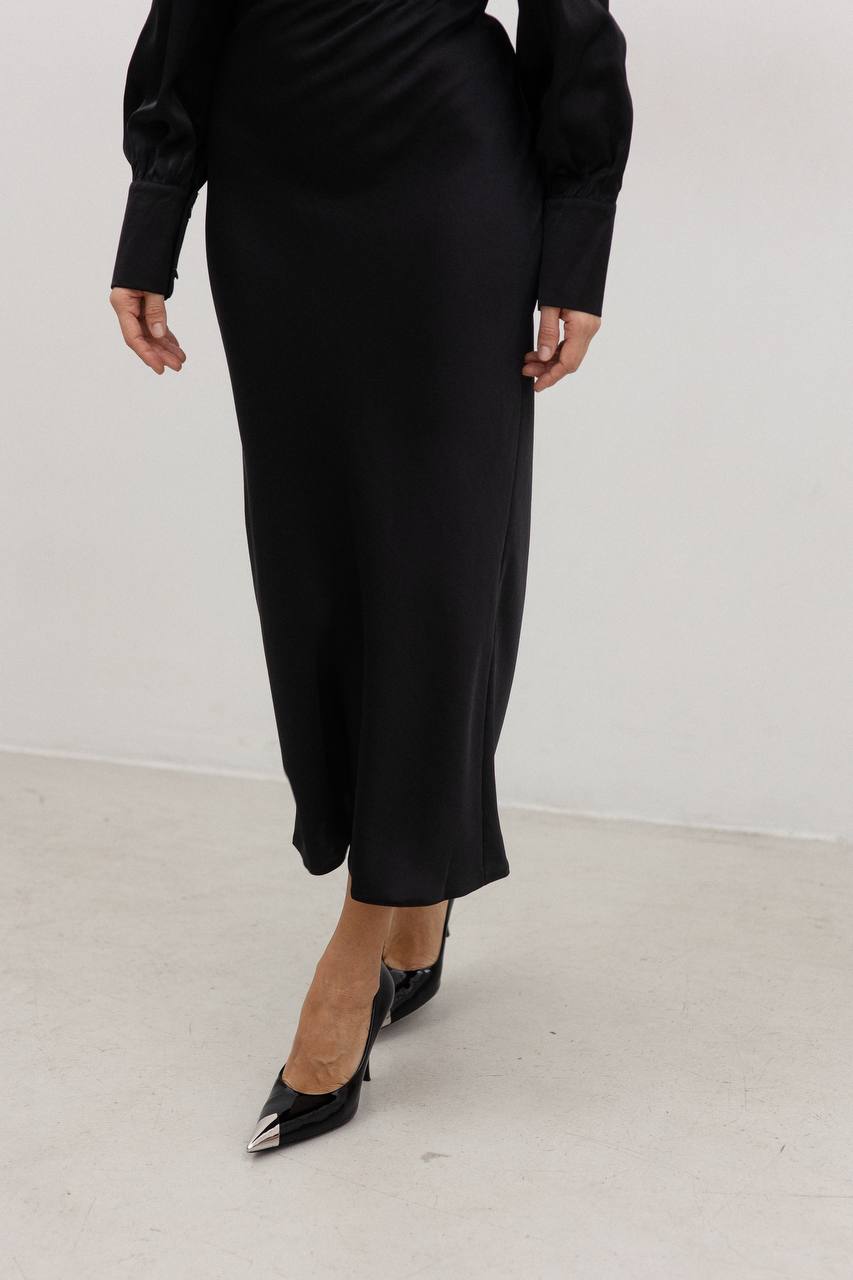 Person wearing a black outfit with a skirt and black shoes on a white background