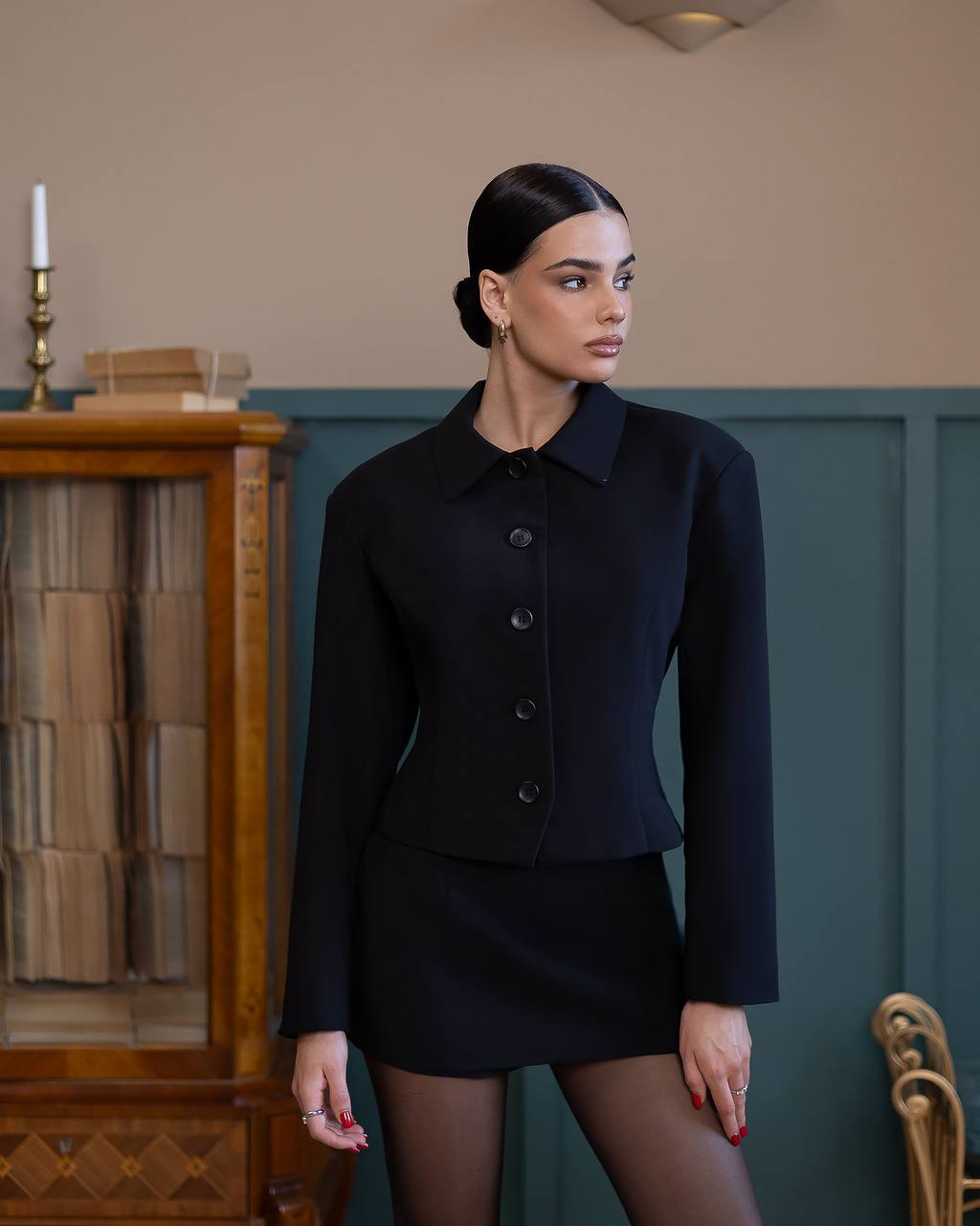 Woman wearing a black outfit standing in a room with a wooden cabinet and candle.