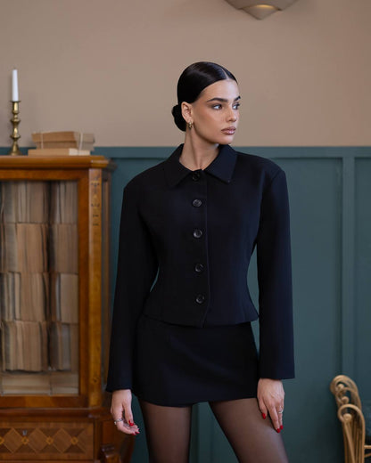 Woman wearing a black outfit standing in a room with a wooden cabinet and candle.