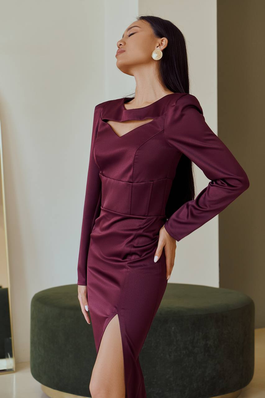 Woman wearing a burgundy dress with cut-out details, standing against a neutral background.