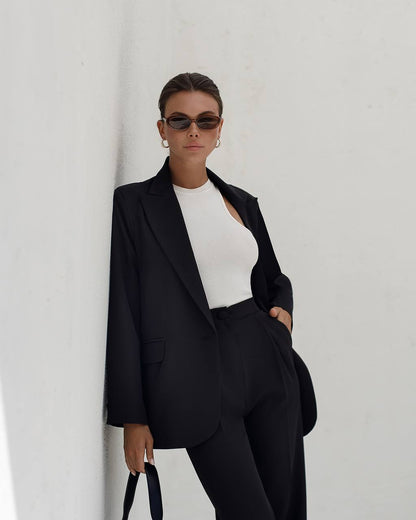Person wearing a black suit and white top against a plain background