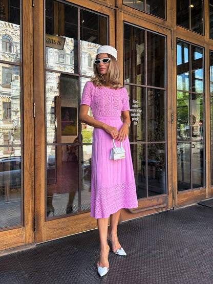 Woman in a pink dress standing in front of large glass doors.