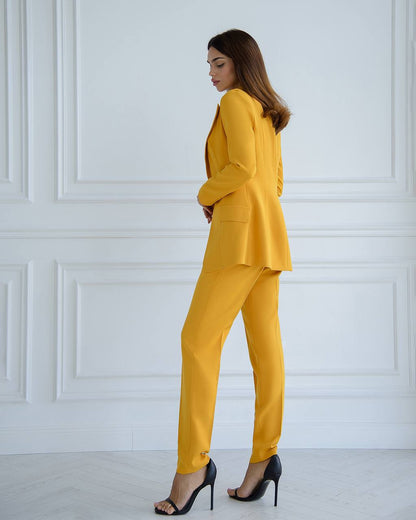 Woman wearing a yellow suit standing against a white paneled wall.