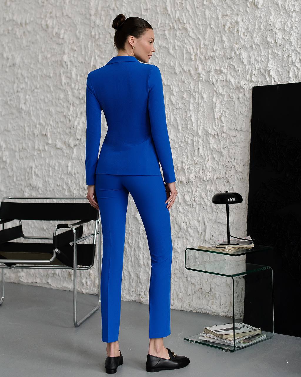 Woman in a blue suit standing in a modern room with a textured white wall.