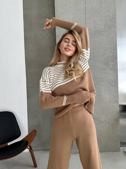 Woman wearing a brown and beige striped sweater and pants in a minimalistic room.