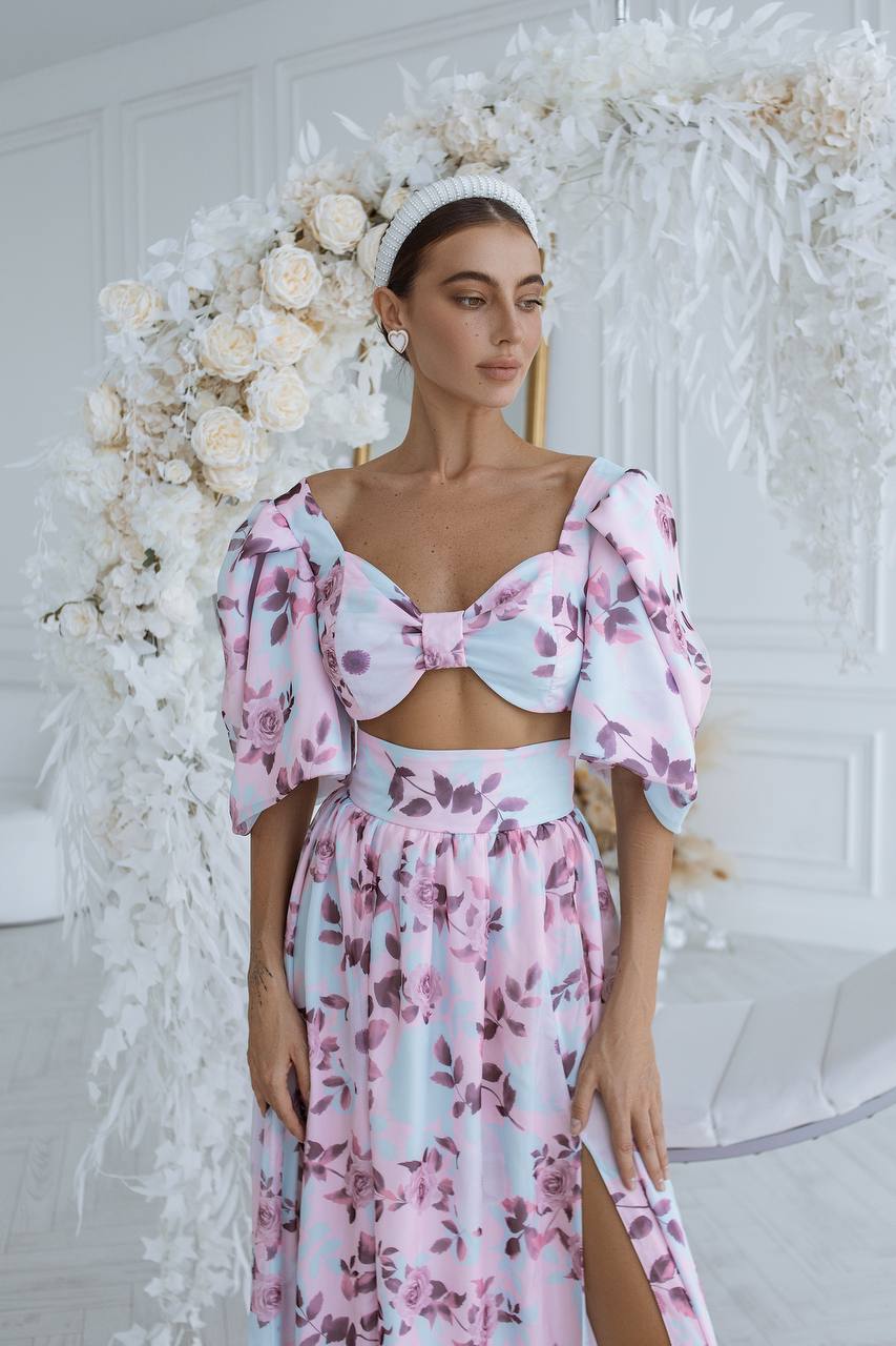 Woman in a floral dress standing in front of a decorative white flower arrangement.