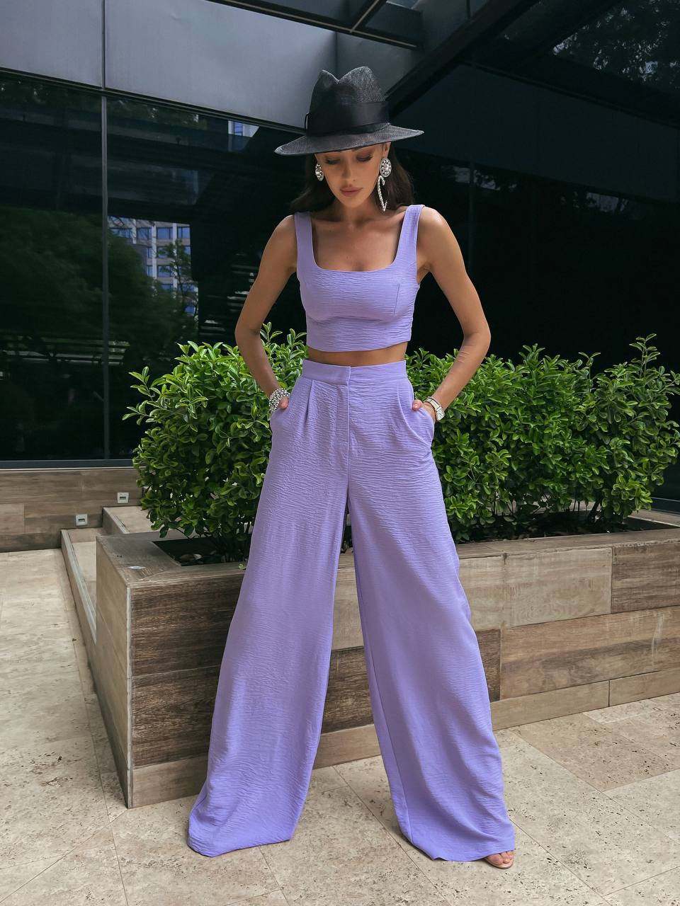 Woman in a lavender outfit standing outdoors with greenery in the background