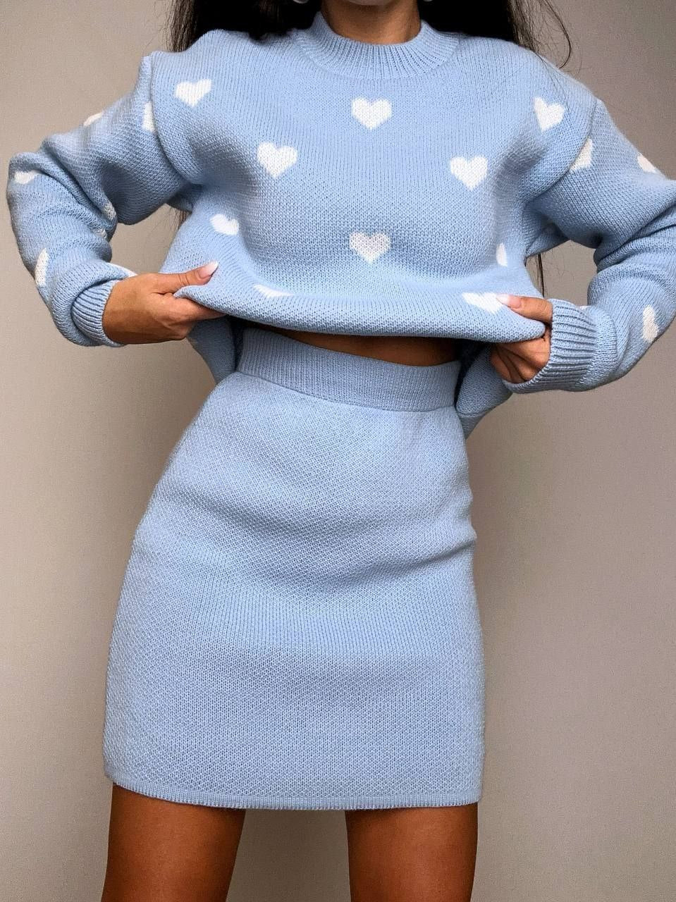 Person wearing a light blue sweater and skirt set with heart patterns against a neutral background