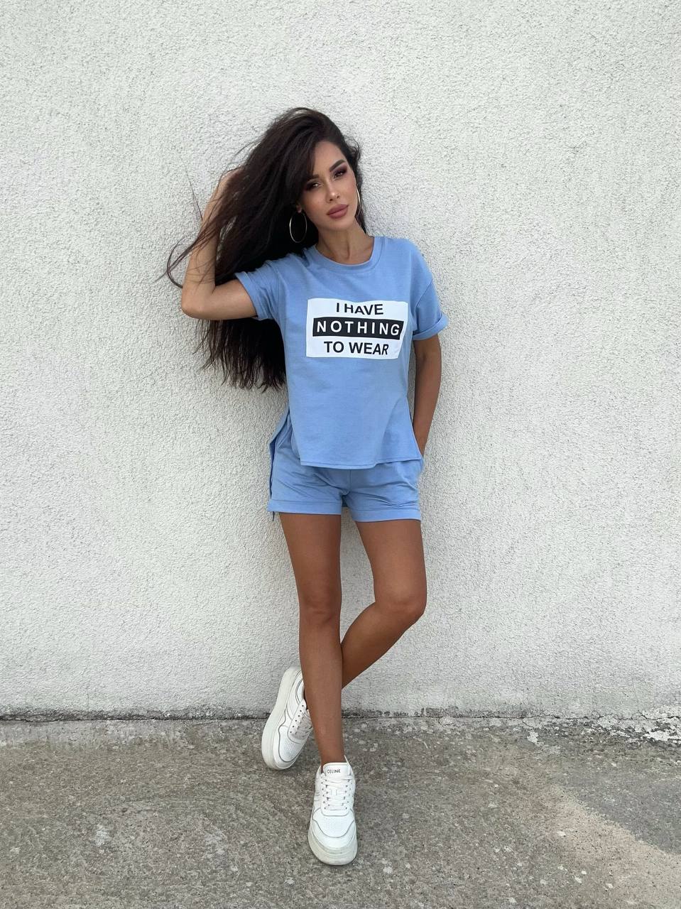 Woman wearing a blue t-shirt with text and matching shorts against a gray wall.