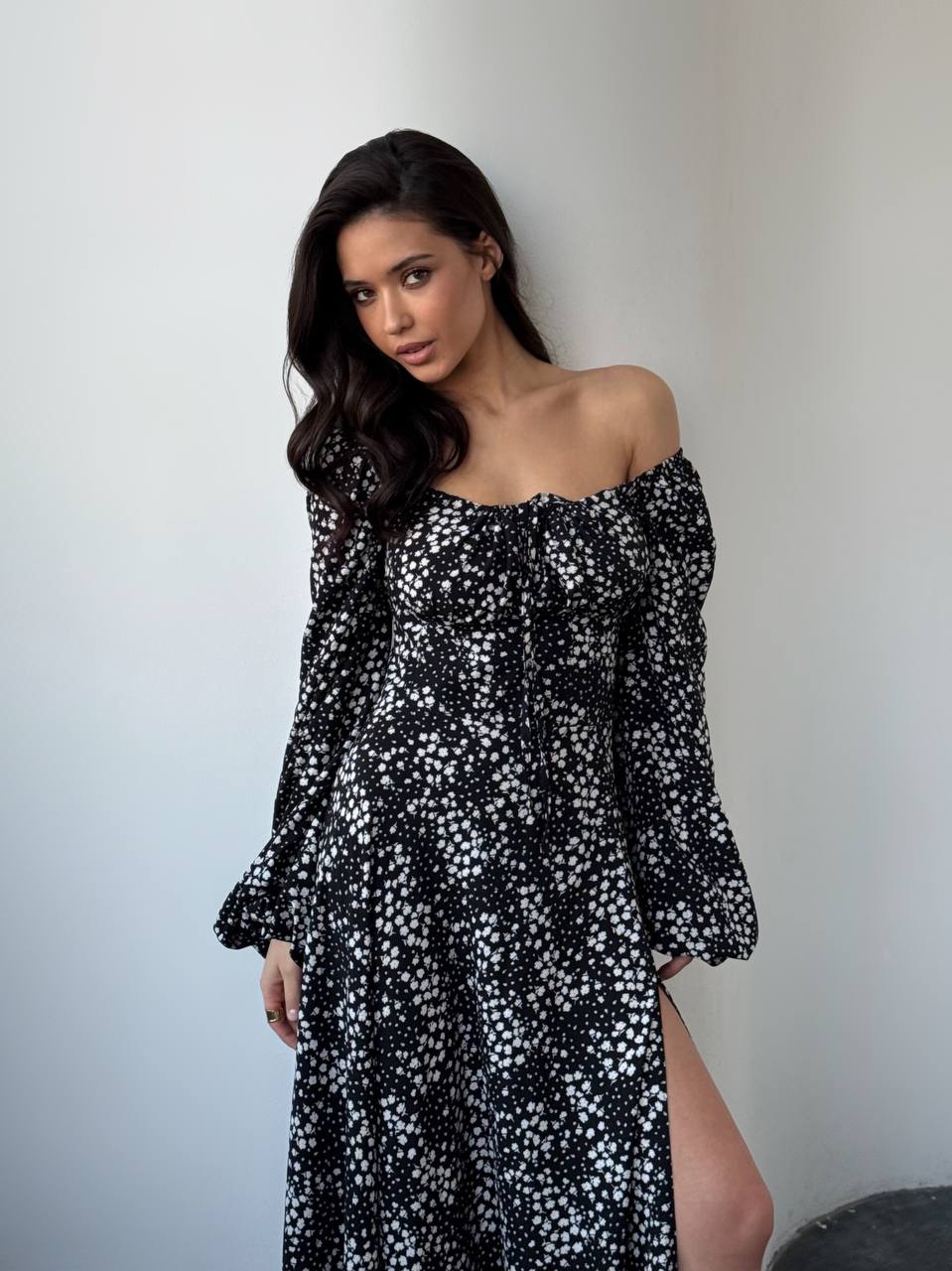 Woman wearing a black floral off-shoulder dress against a plain background