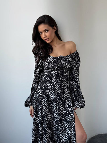 Woman wearing a black floral off-shoulder dress against a plain background