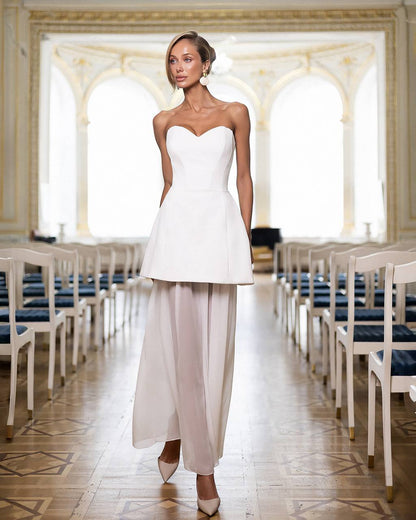 Woman in a white dress standing in an elegant room with rows of chairs.