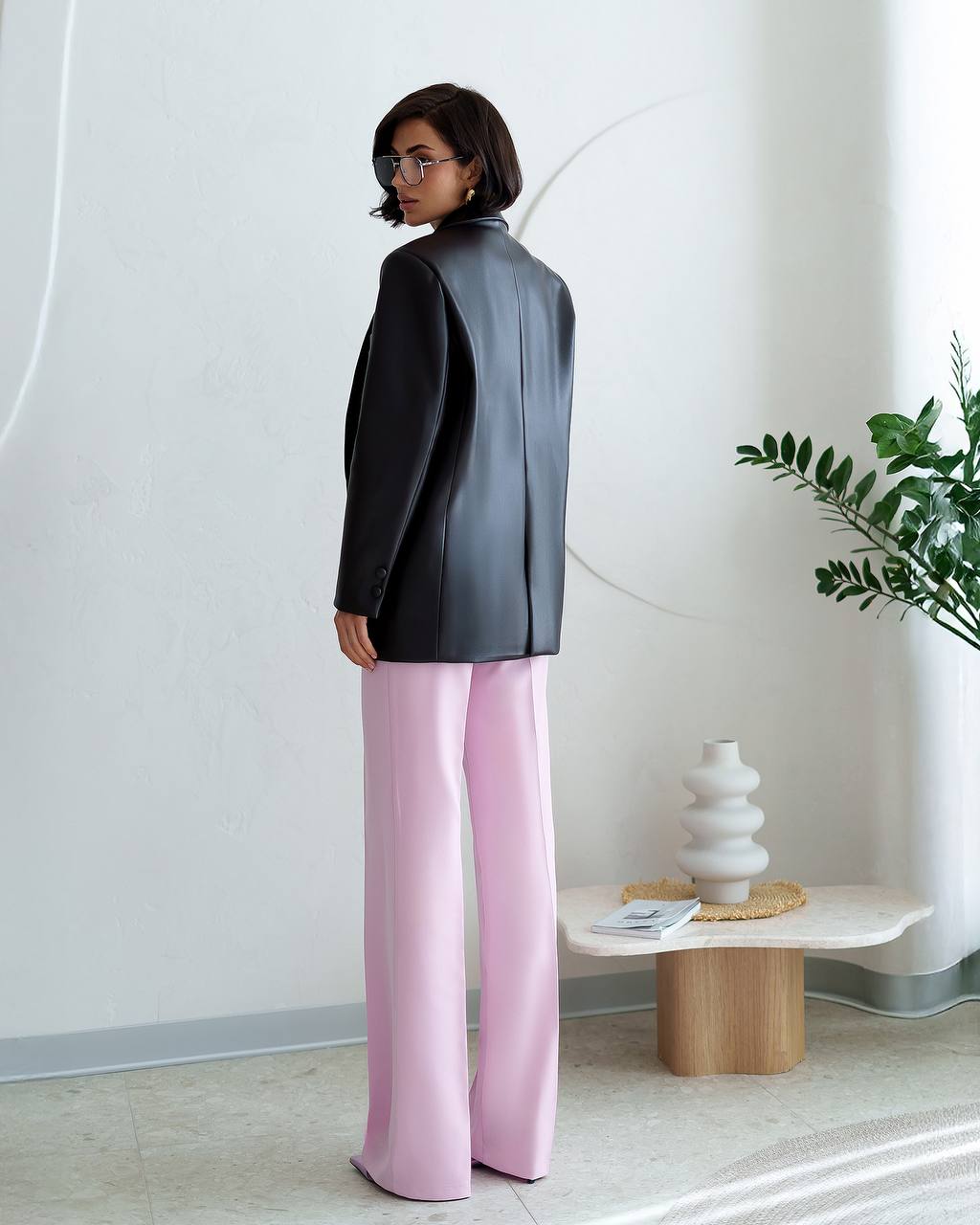 Person wearing a black blazer and pink pants in a minimalistic room.