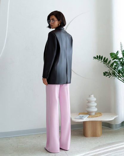 Person wearing a black blazer and pink pants in a minimalistic room.