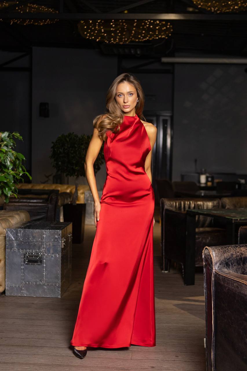 Woman in a red dress standing in a dimly lit room with tables and chairs.
