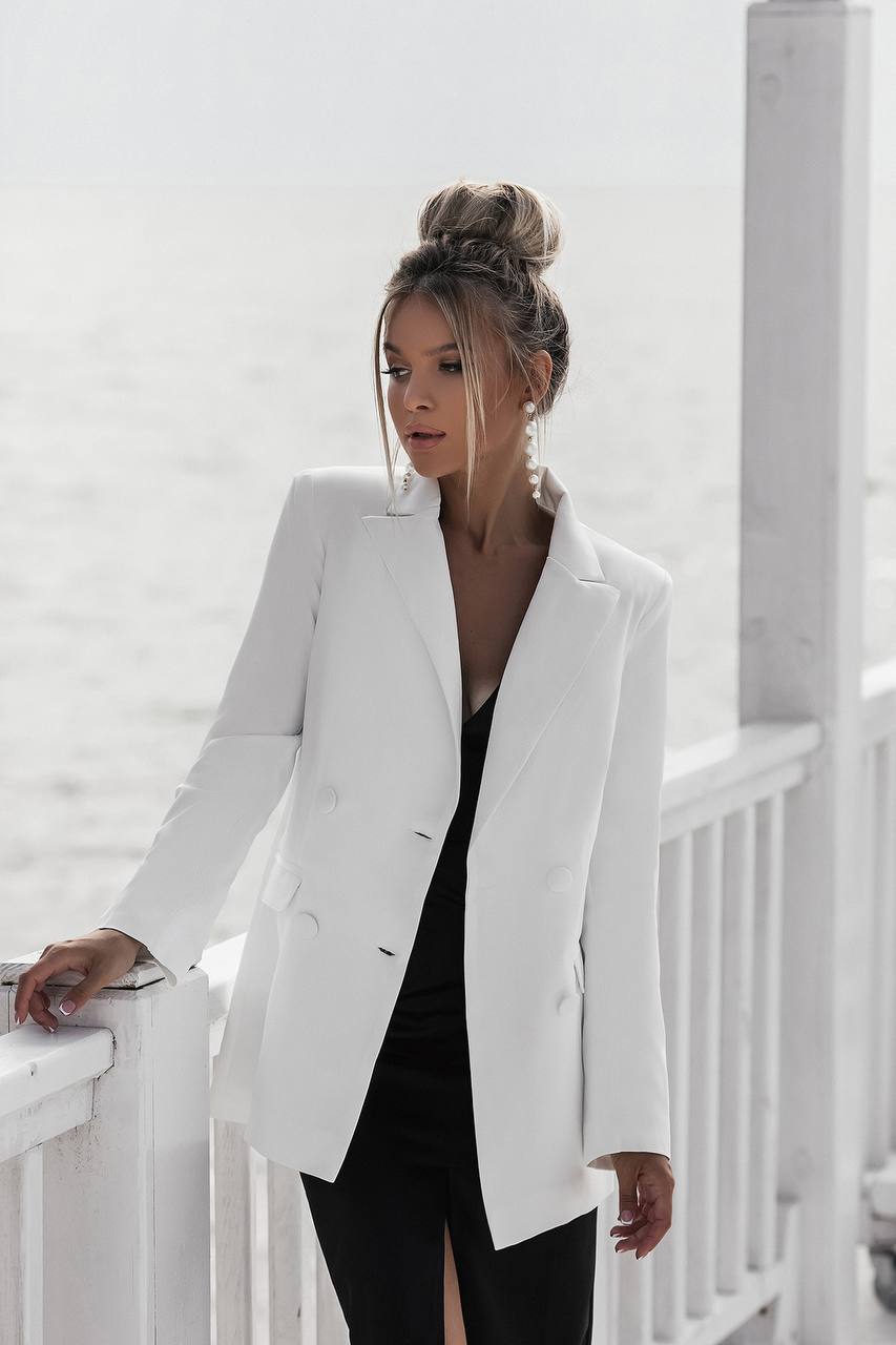 Woman wearing a white blazer over a black dress on a white background