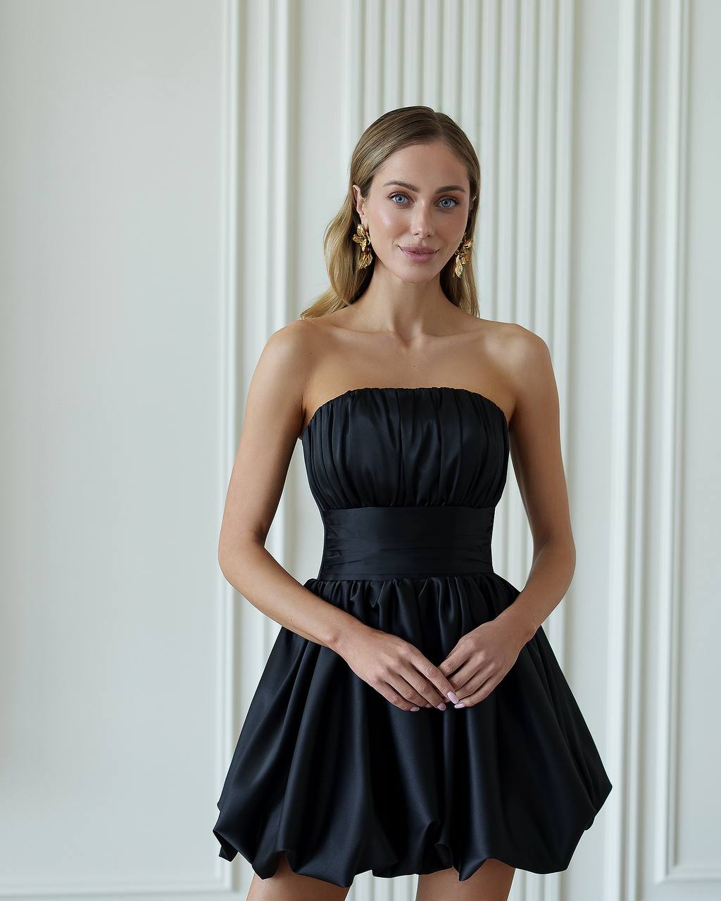 Woman wearing a black strapless dress against a white wall