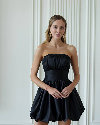 Woman wearing a black strapless dress against a white wall