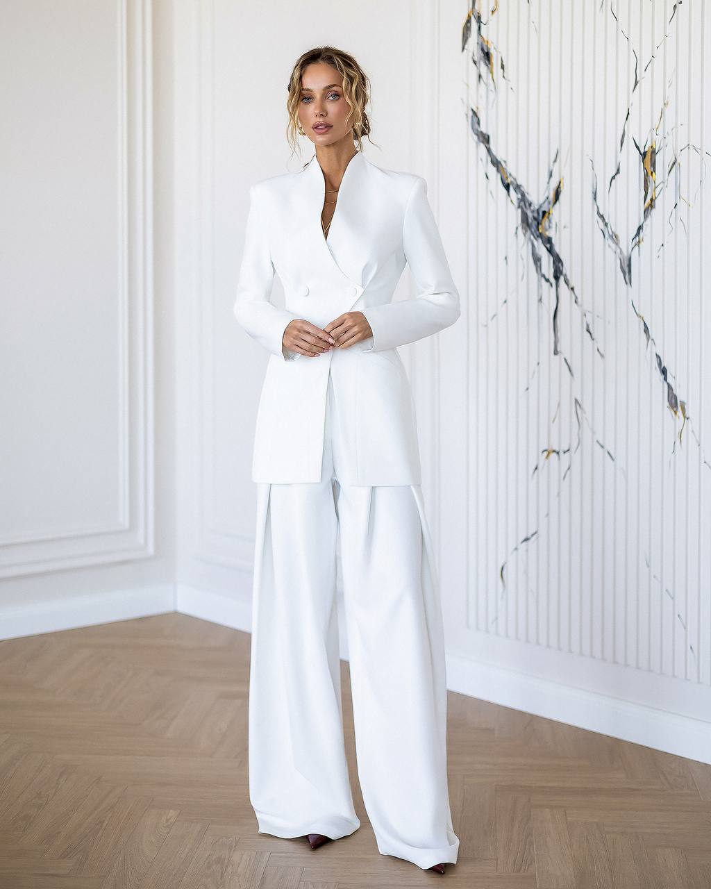 Woman wearing a white suit in a room with marble wall.