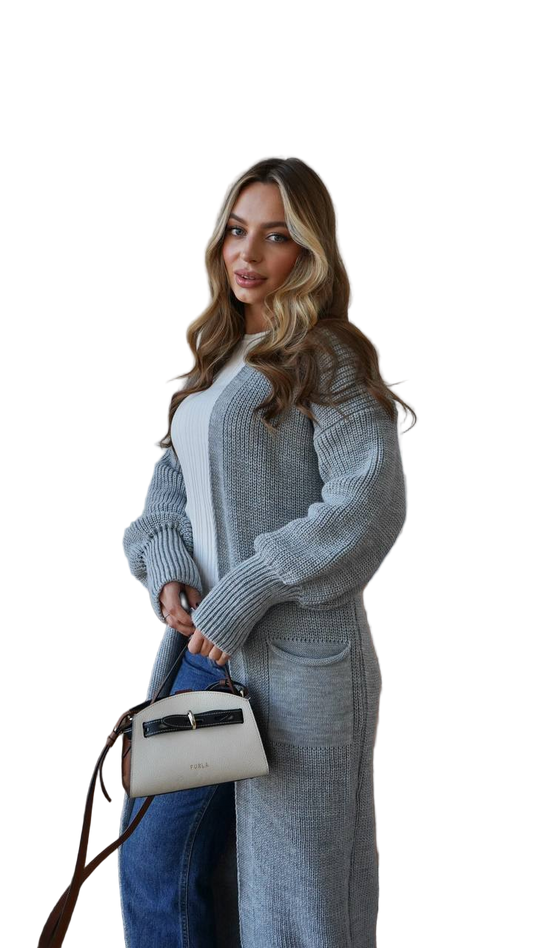 Woman wearing a long gray cardigan over a white top, holding a white handbag with a black strap.