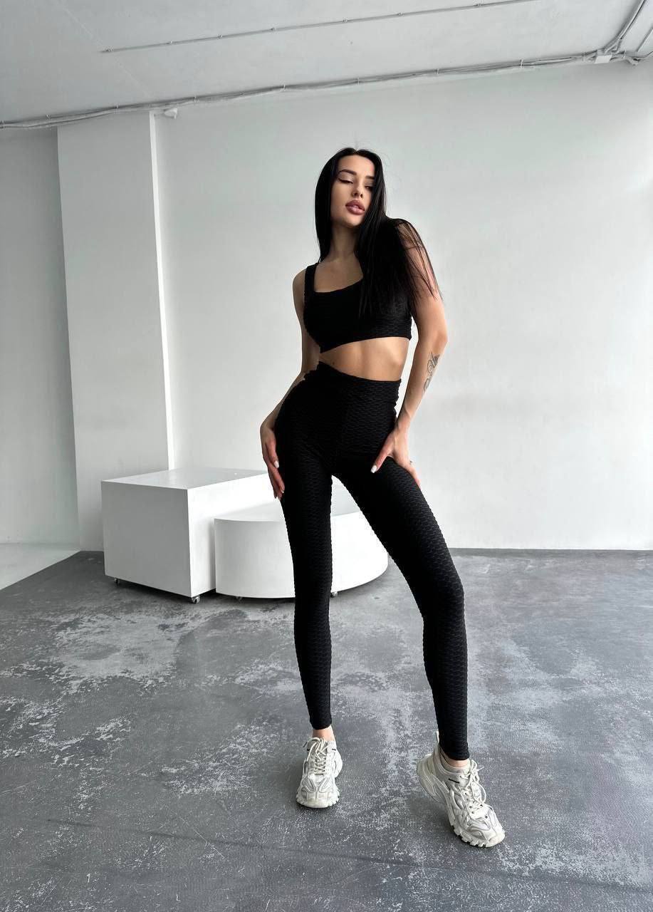 Person wearing a black athletic outfit in a minimalistic room.