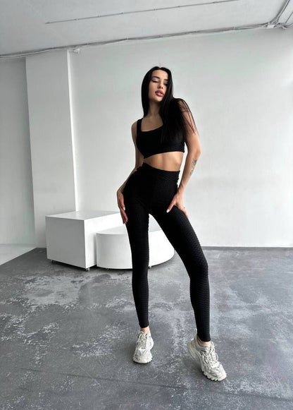 Person wearing a black athletic outfit in a minimalistic room.