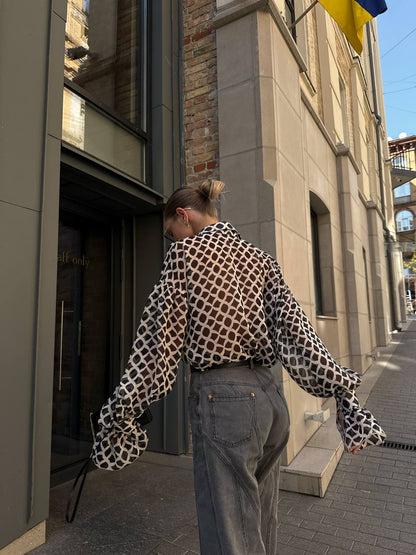 Person wearing a patterned shirt and jeans walking on a city street.