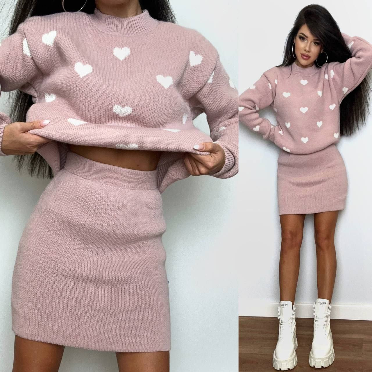 Woman wearing a pink sweater and skirt set with heart patterns, standing against a white wall.